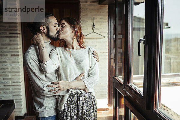 Paar  das sich küsst  während es am Fenster zu Hause steht
