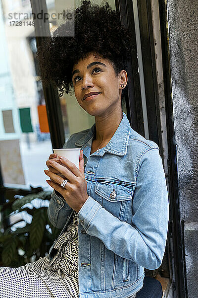 Mittlere erwachsene Frau mit Kaffeetasse  die am Fenster eines Cafés sitzt und nach oben schaut