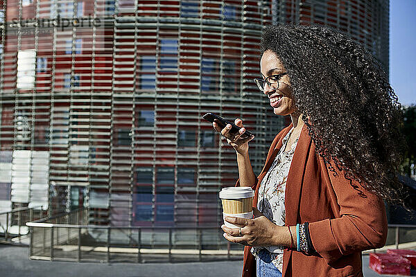 Lächelnde Frau  die eine Voicemail über ihr Smartphone sendet  während sie in der Stadt an einem sonnigen Tag steht