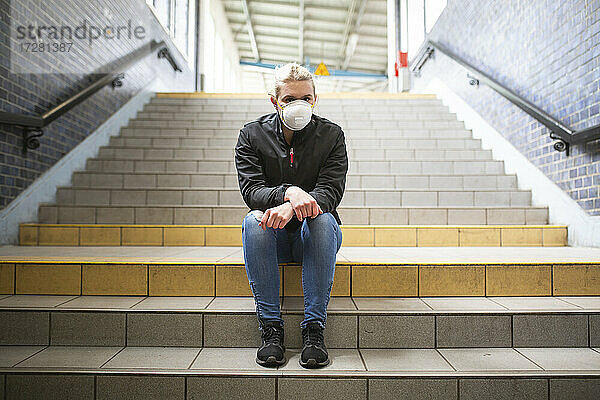 Jugendliches Mädchen mit Schutzmaske und Handschuhen auf der Treppe eines Bahnhofs sitzend