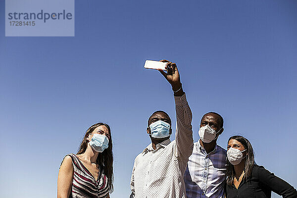 Business-Profis nehmen Selfie mit schützenden Gesichtsmasken gegen klaren blauen Himmel an einem sonnigen Tag