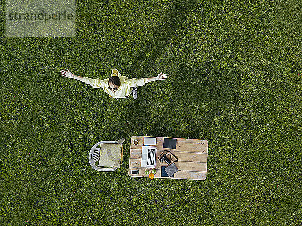 Luftaufnahme einer Frau  die mit erhobenen Armen vor einem Couchtisch auf grünem Rasen steht