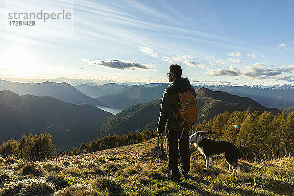 Wanderer mit Hund und Blick auf eine Bergkette bei Sonnenuntergang