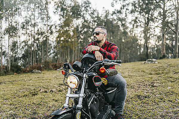 Männlicher Motorradfahrer mit Sonnenbrille auf einem Motorrad im Wald sitzend
