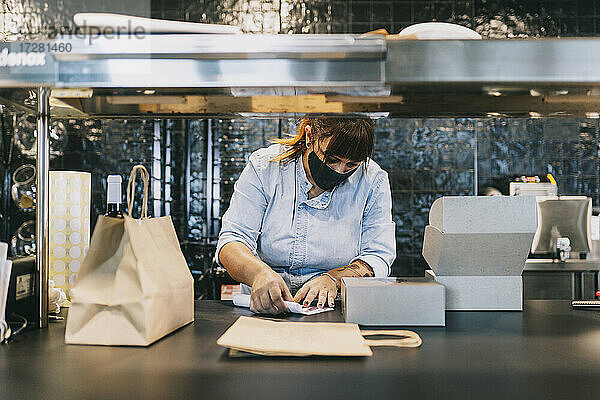 Eine Köchin hält Papier an einem Behälter zum Mitnehmen an der Küchentheke eines Restaurants während COVID-19