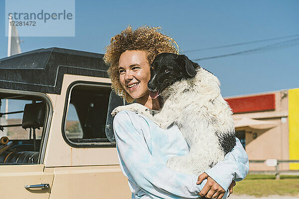 Lächelnde junge blonde Frau mit Hund  die an einem sonnigen Tag wegschaut