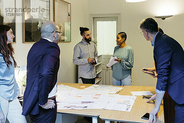 Selbstbewusste Unternehmerin  die am Tisch im Büro mit Kollegen über einen Bauplan diskutiert