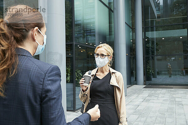 Frauen mit Gesichtsmaske beim Gespräch gegen Bürogebäude