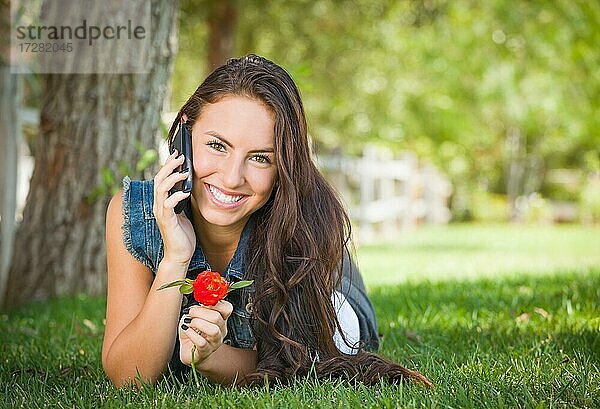 Attraktive glückliche gemischtrassige junge Frau  die draußen im Gras liegend mit dem Handy telefoniert