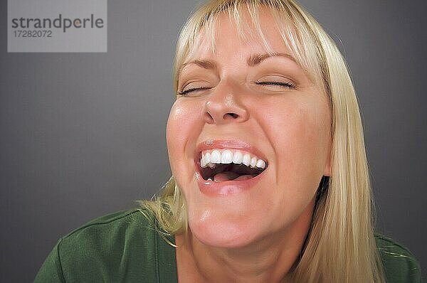 Schöne blonde Frau lachend vor einem grauen Hintergrund