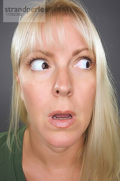 Schockierte blonde Frau mit lustigem Gesicht vor einem grauen Hintergrund