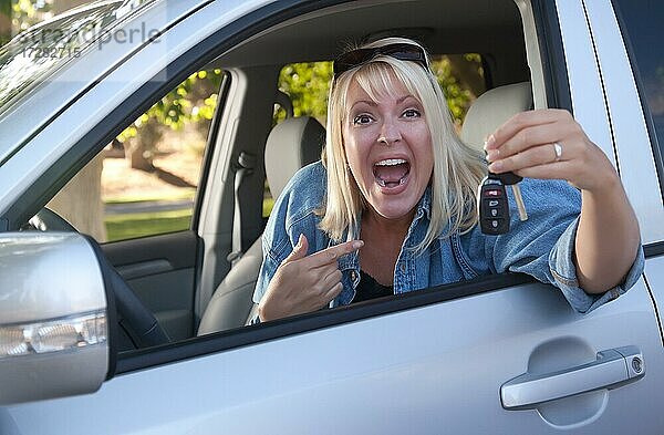 Attraktive glückliche Frau im neuen Auto mit Schlüssel