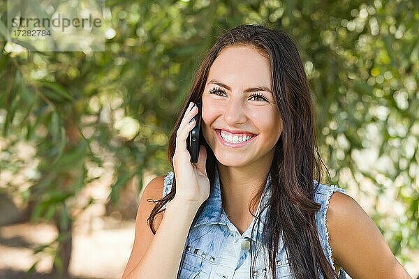 Attraktive glückliche gemischtrassige junge Frau  die draußen mit dem Handy telefoniert