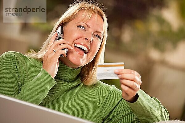 Fröhliche Frau auf ihr Telefon und Laptop mit Kreditkarte