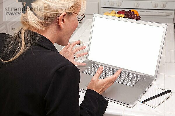 Frau  die in der Küche sitzt und einen Laptop mit leerem Bildschirm verwendet. Der Bildschirm kann mit dem mitgelieferten Beschneidungspfad leicht für eine eigene Nachricht oder ein Bild verwendet werden