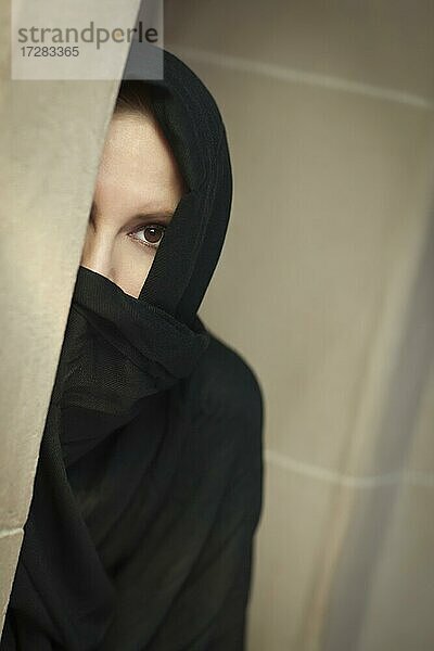 Vorsichtige islamische Frau in einer Fensterscheibe mit traditioneller Burka oder Niqab