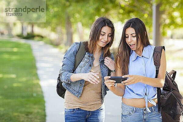 Junge erwachsene gemischtrassige Zwillingsschwestern  die ihre Erfahrungen mit Mobiltelefonen draußen austauschen
