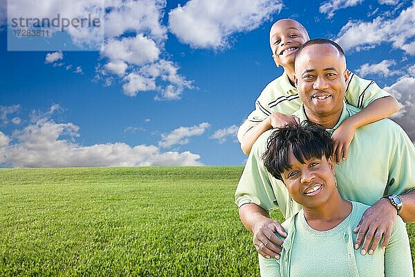 Glückliche afroamerikanische Familie über Grasfeld  Wolken und blauem Himmel  Platz für eigenen Text auf der linken Seite