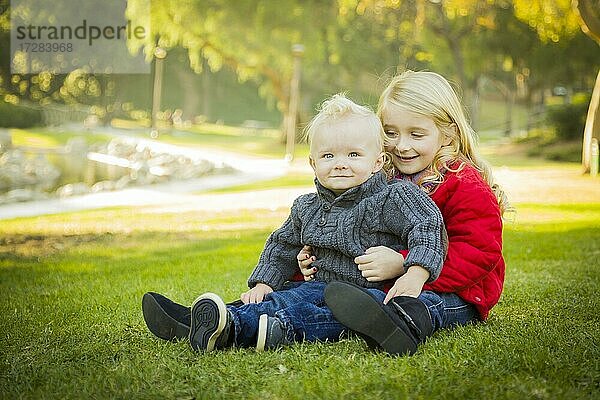 Kleines Mädchen mit ihrem kleinen Bruder tragen Wintermäntel im Freien sitzen im Park