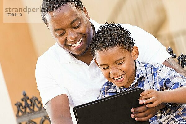 Glücklich afrikanischer amerikanischer Vater und gemischtrassiger Sohn haben Spaß mit Touchpad-Computer-Tablet draußen