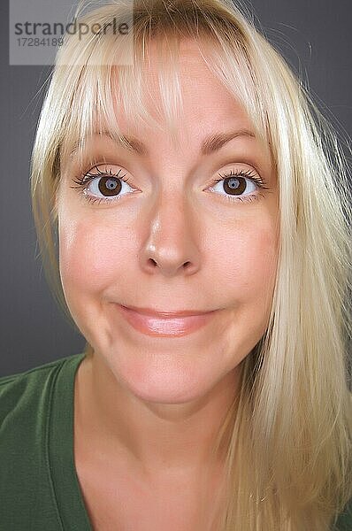 Schöne blonde Frau mit lustigen Gesicht gegen einen grauen Hintergrund