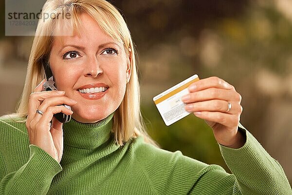 Fröhlich lächelnde Frau verwendet ihr Telefon mit Kreditkarte in der Hand