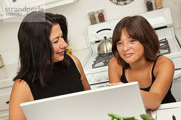 Attraktive hispanische Mutter und gemischt-rassige Tochter in der Küche mit dem Laptop-Computer zusammen