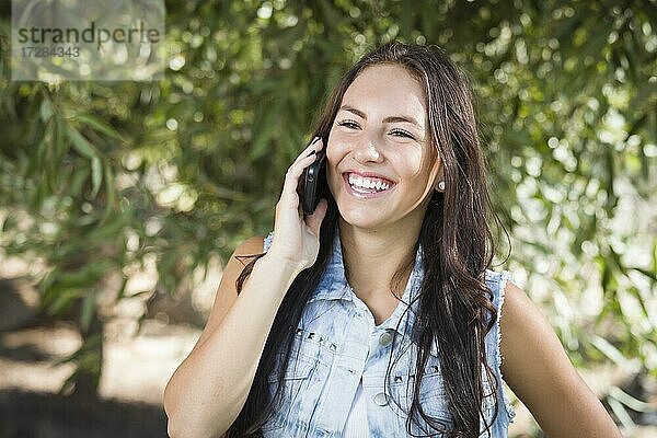 Attraktive glückliche gemischtrassige junge Frau  die draußen mit dem Handy telefoniert