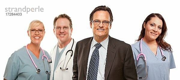 Lächelnde Geschäftsmann in Suite und Krawatte  während männliche und weibliche Ärzte und Krankenschwestern stehen hinter vor einem weißen Hintergrund