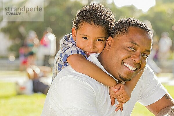 Glücklicher afrikanischer amerikanischer Vater und gemischtrassiger Sohn spielen Huckepack im Park