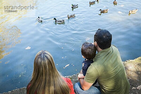 Gemischtrassige Mutter und Vater mit Sohn am Ententeich im Park