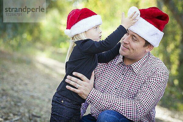 Glücklicher Vater und Tochter mit Spaß tragen santa Hüte im Freien