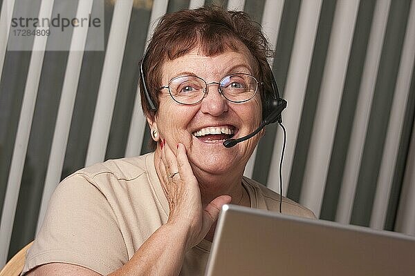 Lächelnde ältere Frau mit Telefon-Headset vor einem Computermonitor