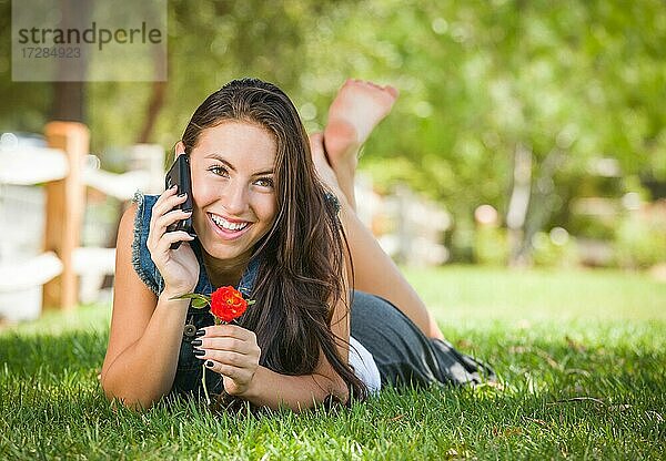 Attraktive glückliche gemischtrassige junge Frau  die draußen im Gras liegend mit dem Handy telefoniert