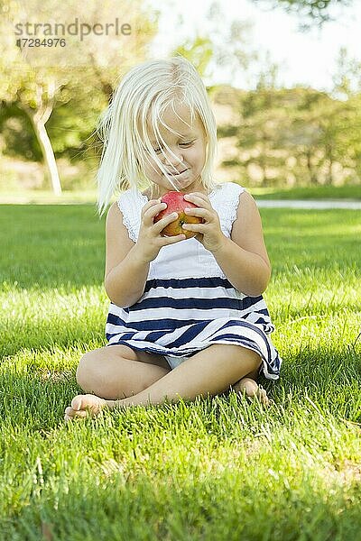 Nettes kleines Mädchen sitzt und ißt Apfel draußen auf dem Gras