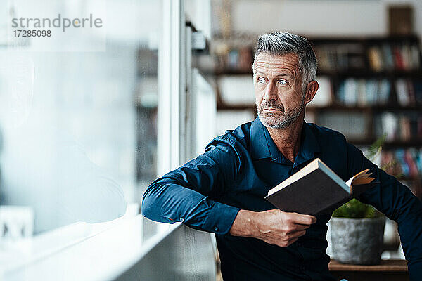 Reifer Geschäftsmann mit Buch  der wegschaut  während er im Café sitzt