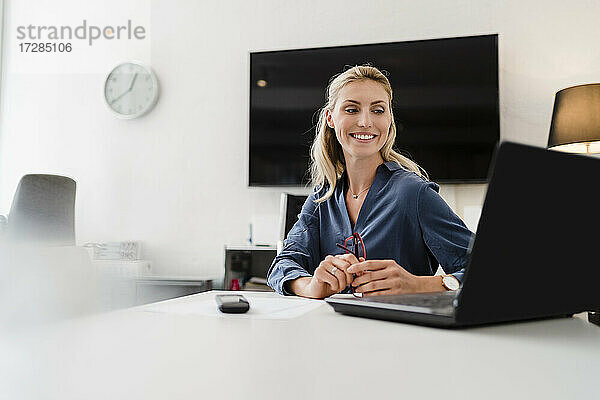 Lächelnde Unternehmerin bei der Arbeit im Büro am Laptop