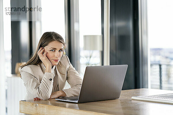 Geschäftsfrau mit Kopf in der Hand vor einem Laptop am Tisch im Büro stehend