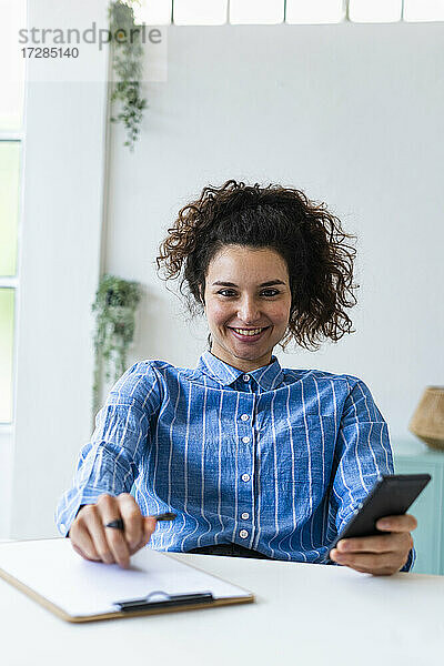 Lächelnde Geschäftsfrau mit Mobiltelefon am Schreibtisch im Büro