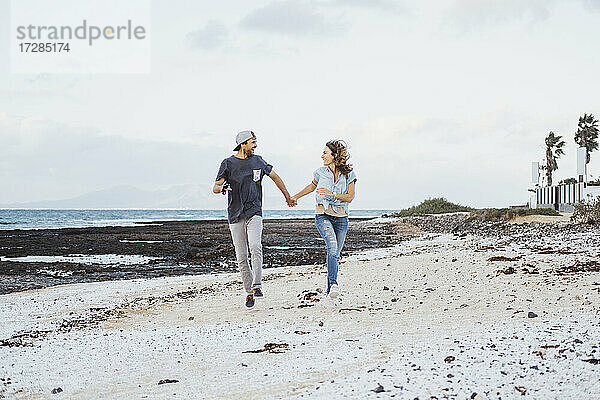 Unbekümmertes Paar  das sich beim Laufen am Strand an den Händen hält