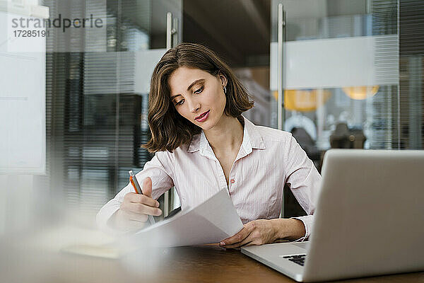 Schöne junge Geschäftsfrau  die ein Dokument liest  während sie am Schreibtisch im Büro sitzt