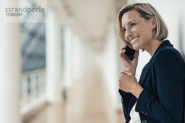 Unternehmerin lächelt  während sie im Büro mit dem Handy telefoniert