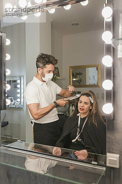 Spiegelreflexion eines männlichen Experten  der einer Kundin im Salon die Haare färbt