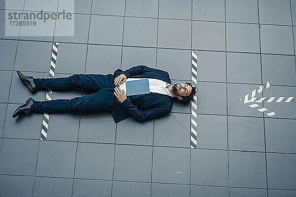 Geschäftsmann mit digitalem Tablet auf dem Boden ruhend mit Pfeilsymbol im Büro
