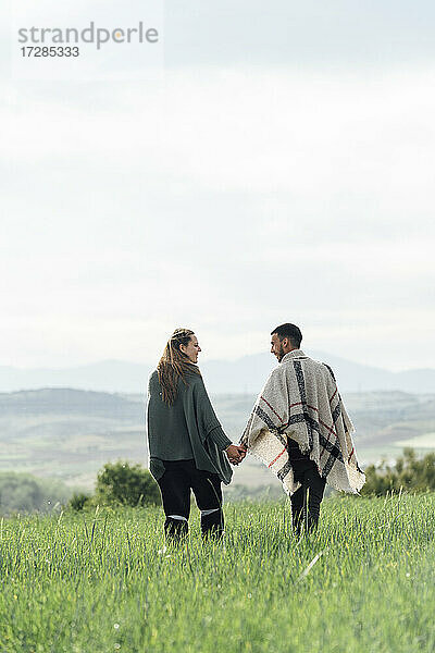 Junges Paar hält sich an den Händen  während sie zusammen auf einem Feld spazieren gehen