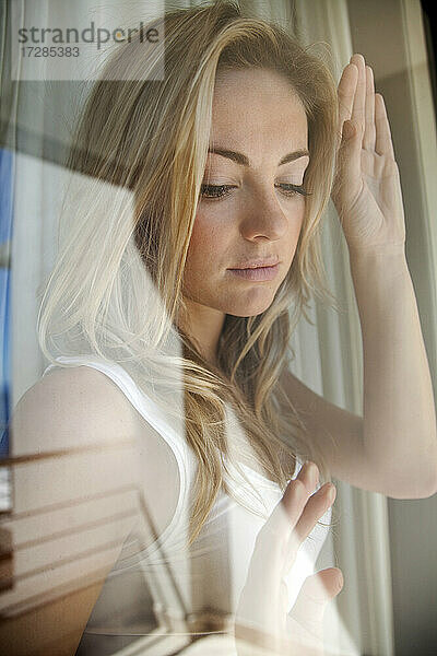 Blonde junge Frau durch Fensterscheibe zu Hause gesehen