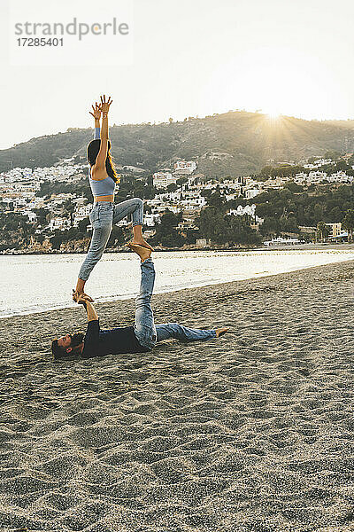 Frau balanciert auf einem Mann  während sie am Strand trainiert