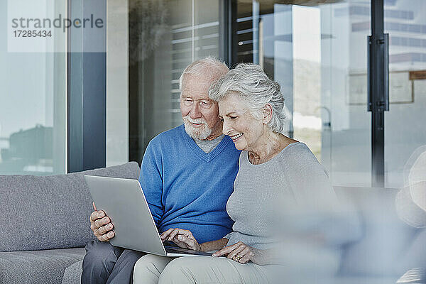 Lächelndes älteres Paar mit Laptop im Wohnzimmer zu Hause