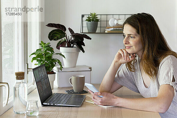 Lächelnde weibliche Fachkraft bei einem Videogespräch am Laptop im Büro zu Hause