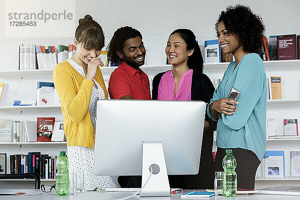 Männliche und weibliche Fachkräfte lächelnd vor einem Computer im Büro